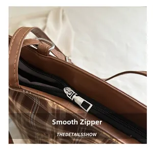 Close-up of smooth silver metal zipper and brown plaid fabric texture on a tote bag