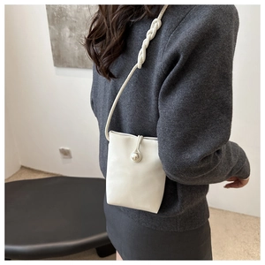 Detail of a cream mini shoulder bag with large pearl button and braided strap texture