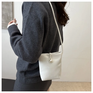 Detailed view of mini white leather bucket bag with a large pearl clasp and shoulder strap