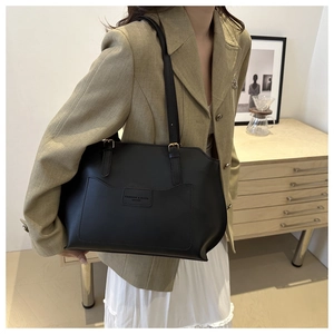 Détail du sac cabas minimaliste en cuir noir avec poche frontale et finitions dorées