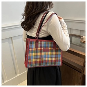 Detail of multi-color plaid tote bag with red leather trim on a female model