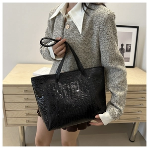 Détail d'un grand sac cabas noir à motif crocodile brillant tenu par un mannequin