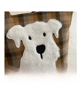 Macro detail of brown plaid fabric and a plush white dog appliqué on a fashion tote bag