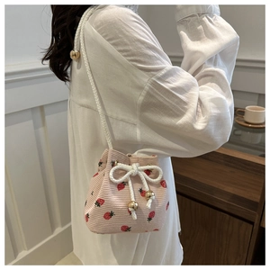 Detail of pink corduroy bucket bag featuring red strawberry prints and white drawstrings