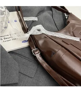 Detail of dark brown tote bag with glossy leather texture, lace decor and metal buckle