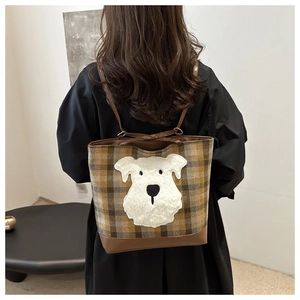 Detail of plaid tote bag featuring a plush schnauzer patch and brown leather straps