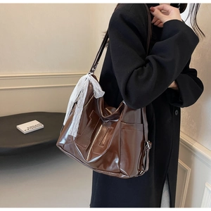 Deep brown faux leather tote bag with H-pattern and white lace bow detail shown on shoulder
