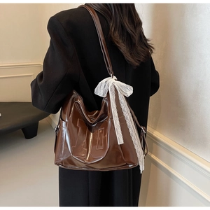 Detail of glossy brown tote bag featuring embossed texture and white lace bow accessory