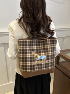 Plaid canvas tote bag with embroidered puppy detail and brown leather base worn by a model