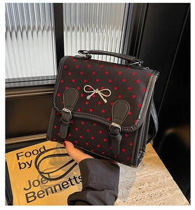 Detail of black backpack with red heart embroidery and silver bow buckle accessory