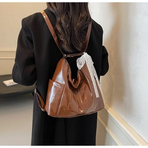 Brown PU leather backpack with lace ribbon detail shown worn with a long black coat