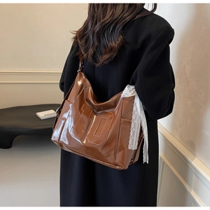 Detail view of large brown glossy tote bag with lace ribbon on black wool coat