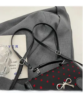 Detail of black crossbody bag with red heart patterns and silver bow clasp on grey blazer