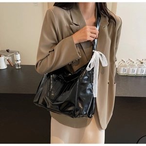 Detail of glossy black patent leather tote with H-patch and white lace bow accessory