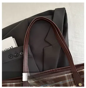 Detail of plaid tote bag featuring brown leather handles and premium stitching work