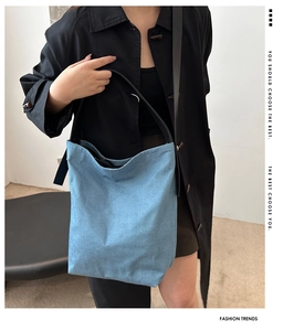 Detail of light blue denim tote bag featuring black leather straps and casual slouchy texture