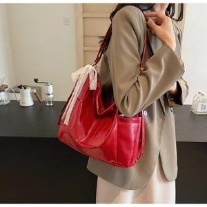 Close-up of a large red leather tote bag featuring a white lace bow and side pocket detail