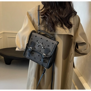 Close-up of grey textured crossbody bag with bow patterns and silver buckle detail