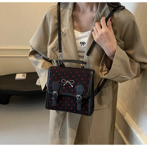 Detail of black fabric crossbody bag featuring red heart patterns and silver metal bow