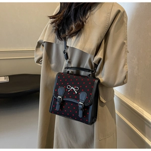 Detail of black fabric crossbody bag with red heart pattern and silver bow decoration