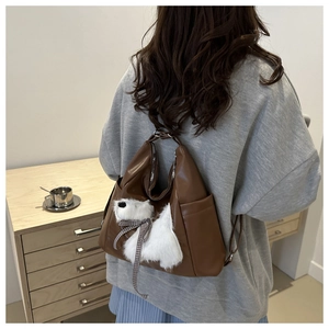 Rear view of a model wearing the brown leather tote bag with a plush puppy charm
