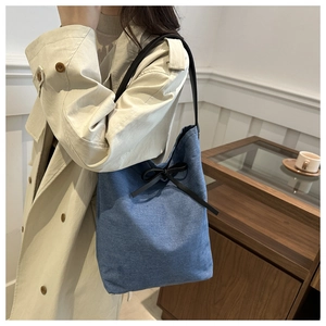 Detail of blue denim tote bag featuring a decorative black bow and slim leather strap