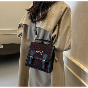 Close-up of black crossbody bag with red heart pattern and silver bow detail