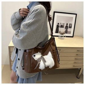 Detail of a brown PU leather shoulder bag with a white plush puppy and plaid bow
