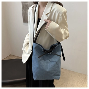 Detail of blue denim bucket bag featuring a black bow and premium leather strap