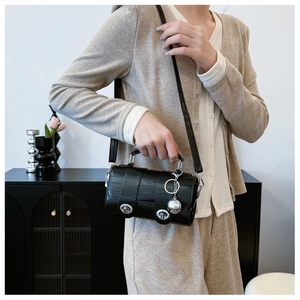 Detail of black cylindrical crossbody bag with crocodile texture and silver clasps