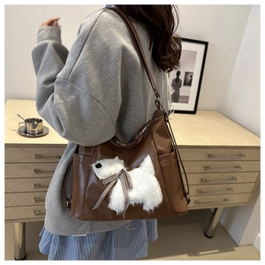 Detail view of brown faux leather tote featuring a plush dog with a checkered bow