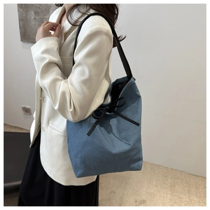 Close-up of blue denim tote bag with black ribbon bow and leather strap on model