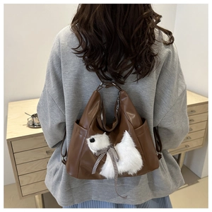 Detailed back view of a brown leather backpack with a cute white dog plush pendant