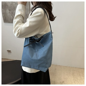Detail of blue denim bucket bag featuring a black bow and sleek shoulder strap