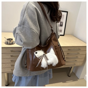 Detail of brown leather shoulder bag featuring a white plush dog charm with a bow
