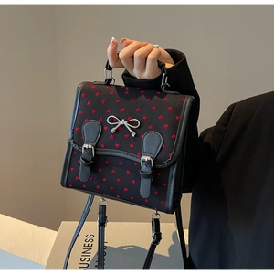 Detail of black fabric bag featuring red heart patterns and silver metal bow ornament
