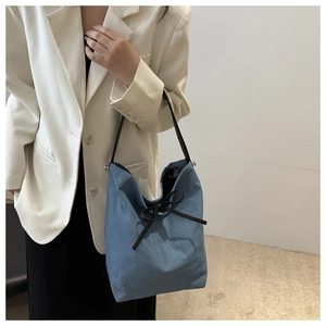 Detail of light blue denim bucket bag featuring black bow ties and silver metal studs