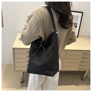 Detail of black denim bucket bag with leather drawstring bow on model in casual outfit
