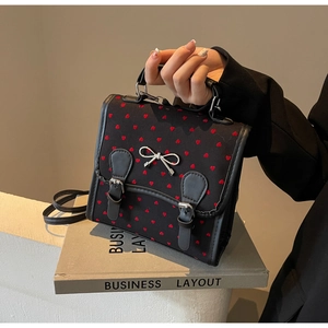 Detail of black knit bag with red hearts featuring silver bow and buckle straps