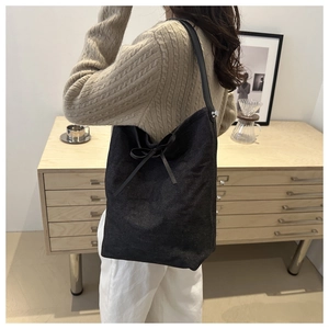 Close-up of a large black denim bucket bag with a delicate bow and leather shoulder strap