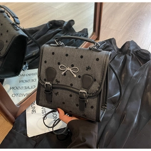 Detail of grey plaid bag with black polka dots and a silver bow on the flap