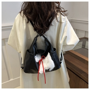 Detail of black multi-functional backpack with white puppy pendant and red bow accessory