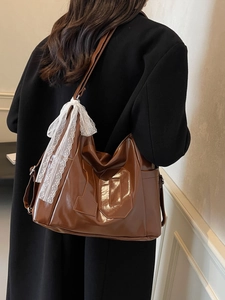 Brown glossy leather tote bag with lace bow and number ten detail worn by a model