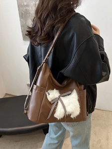 Brown leather shoulder bag with plush dog decor and large capacity shown on model
