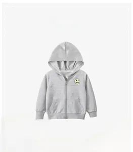 Détail d'un sweat à capuche gris pour enfant avec écusson sourire jaune et fermeture éclair