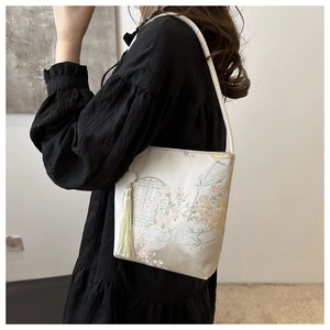 Detail of white silk brocade bag with floral patterns and side tassel on model
