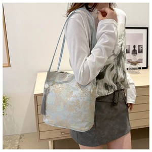 Detail of light blue embroidery tote bag with gold floral jacquard and grey tassel charm