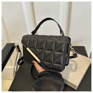 Detail of a black quilted handbag with asymmetric gold bar and elegant chain strap