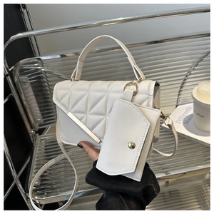 Detailed view of white quilted crossbody bag with gold metal trim and mini charm pouch