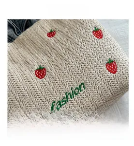 Close-up of beige woven tote bag with red strawberry embroidery and green fashion lettering